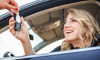 Young woman smiling, being handed car keys to her first vehicle