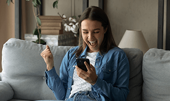 Young woman on the couch with her cell phone happy and excited