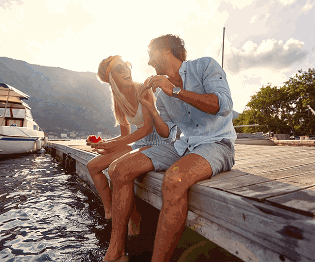 Couple smiling while sitting on a dock next to a boat.
