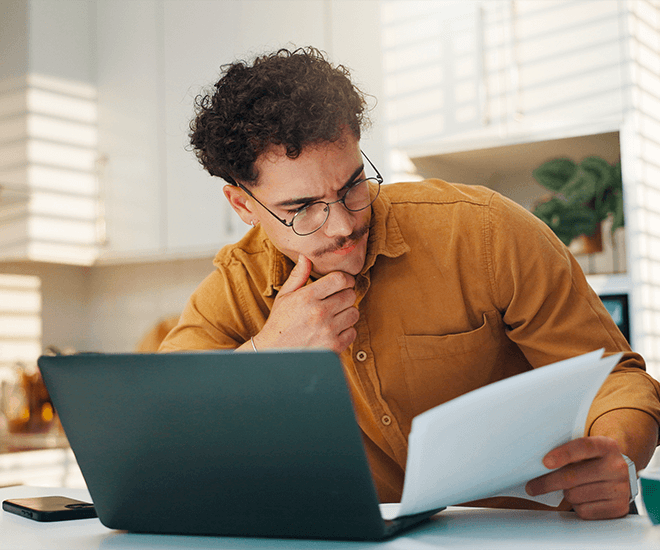 A man looking at papers while on his laptop.
