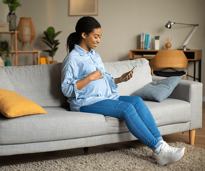 Pregnant woman sitting on couch smiling at phone.