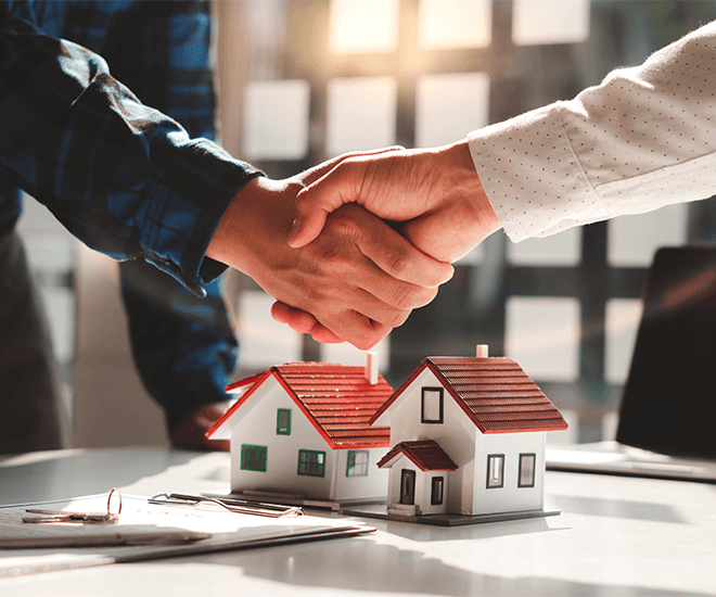 People shaking hands over a model of a house.