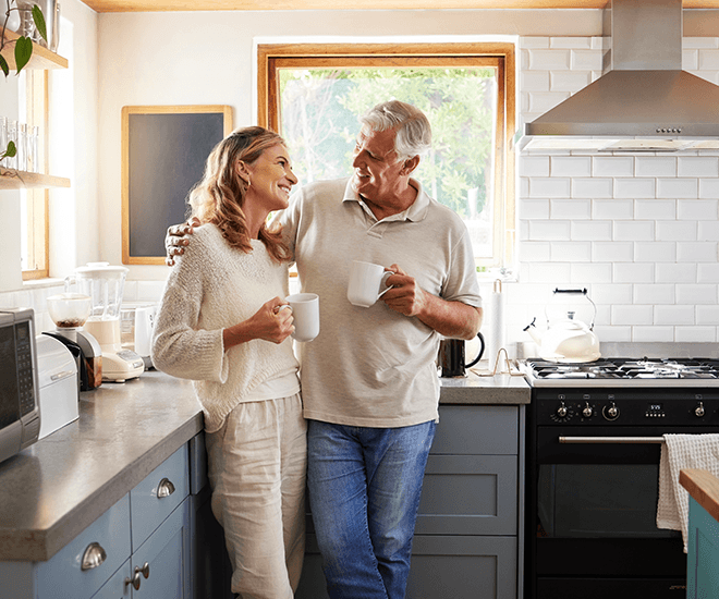 Older couple smiling a drinking coffee together in their kitchen.