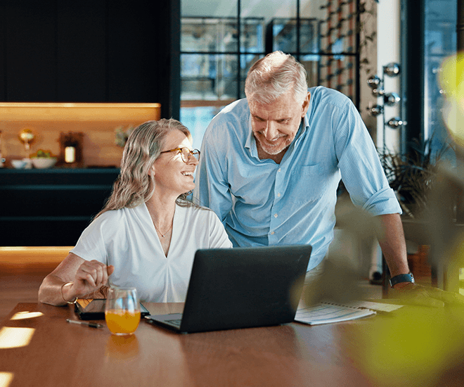 Older couple smiling while on laptop in their kitchen.