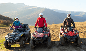 3 people wearing helmets and sitting on ATVs in the mountains
