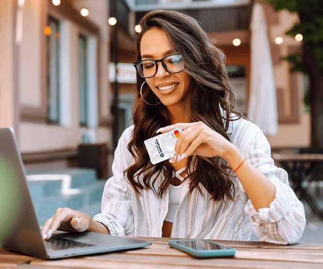 Woman smiling looking at laptop holding debit card.