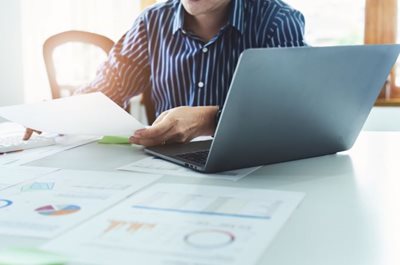 Man on computer looking at charts on papers