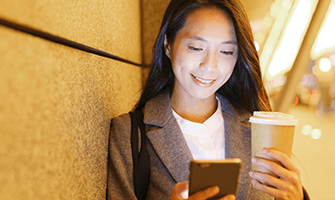 Asian business woman looking at her phone, smiling, holding a cup of coffee
