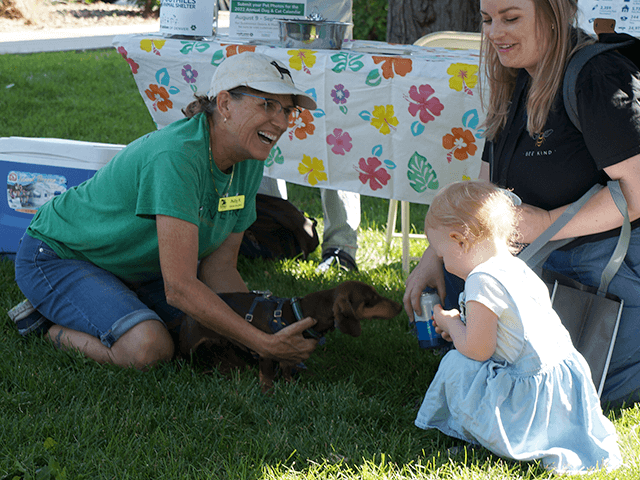 Little girl and mom petting a small dog being held by a Foothills Animal Shelter employee
