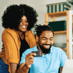 A smiling couple holding a CUD Platinum Credit Card while on their laptop.