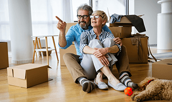 Elderly couple sitting on the floor next to their moving boxes