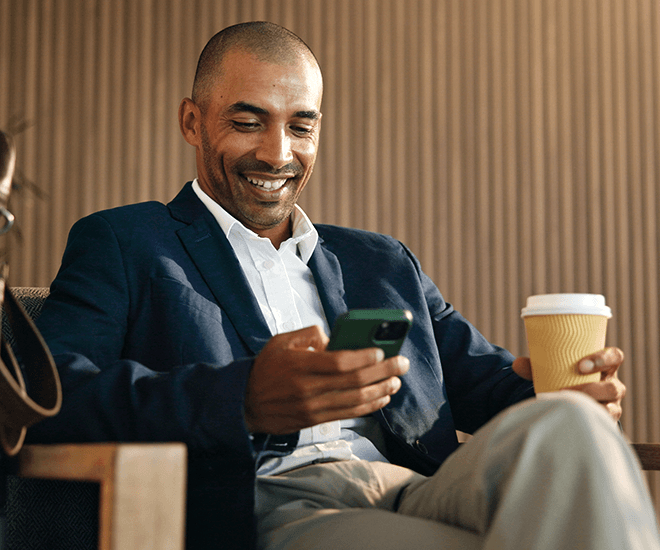 Smiling man sitting down with a coffee looking at his phone.