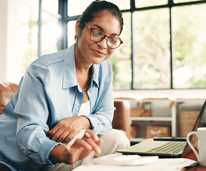 Smiling woman using a calculator while also using a laptop.