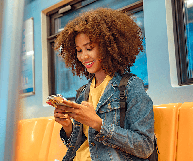 Happy woman sitting in public transport looking at her cell phone.