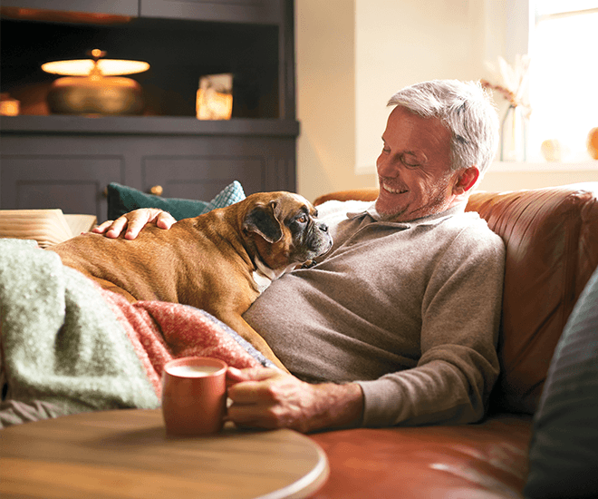 A smiling man laying on the couch with his dog.