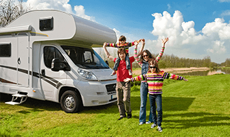 Excited family with their arms outstretched standing in front of their RV on a nice, sunny day