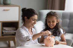 mom and daughter put coins in piggy bank